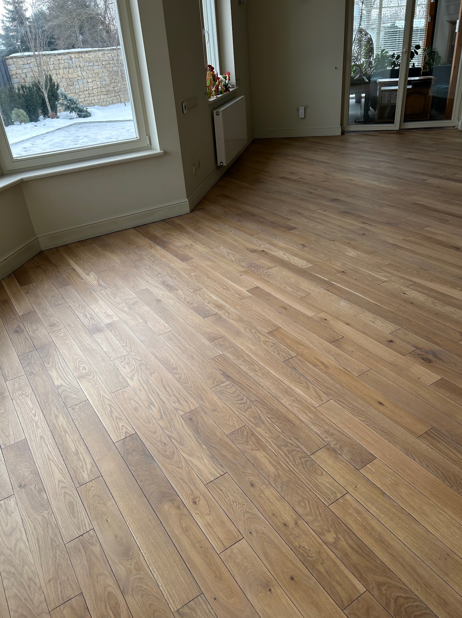 Ułożony parkiet w jodełkę francuską, widok z góry, naturalne oświetlenie, okno z widokiem na zimowy ogród, jasne ściany, nowoczesny styl.