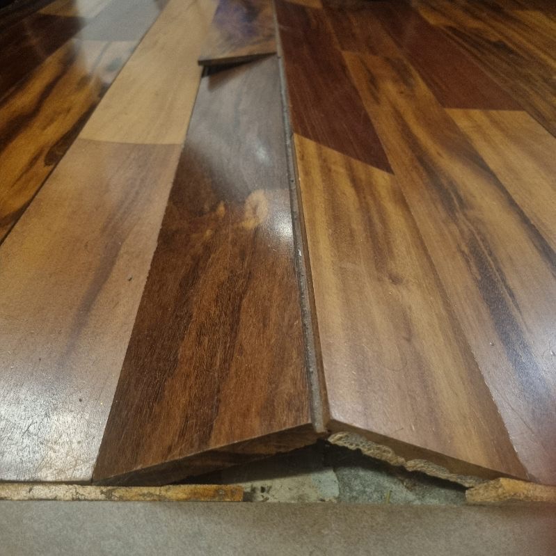 Uszkodzony parkiet z widocznymi ubytkami i odspojonymi elementami. Fragment podłogi z wyraźnymi śladami zużycia i brakiem fragmentu deski. Widoczne podłoże.