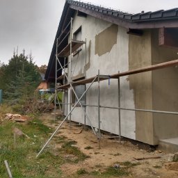 LUISBUD - Dom w trakcie ocieplania elewacji, widoczne rusztowania i częściowo nałożony tynk. Prace w toku, widok z boku budynku, pochmurne niebo.