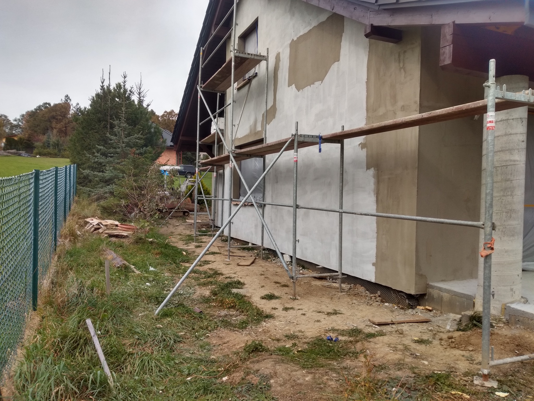 Dom w trakcie ocieplania elewacji, widoczne rusztowania i częściowo nałożony tynk. Prace w toku, widok z boku budynku.