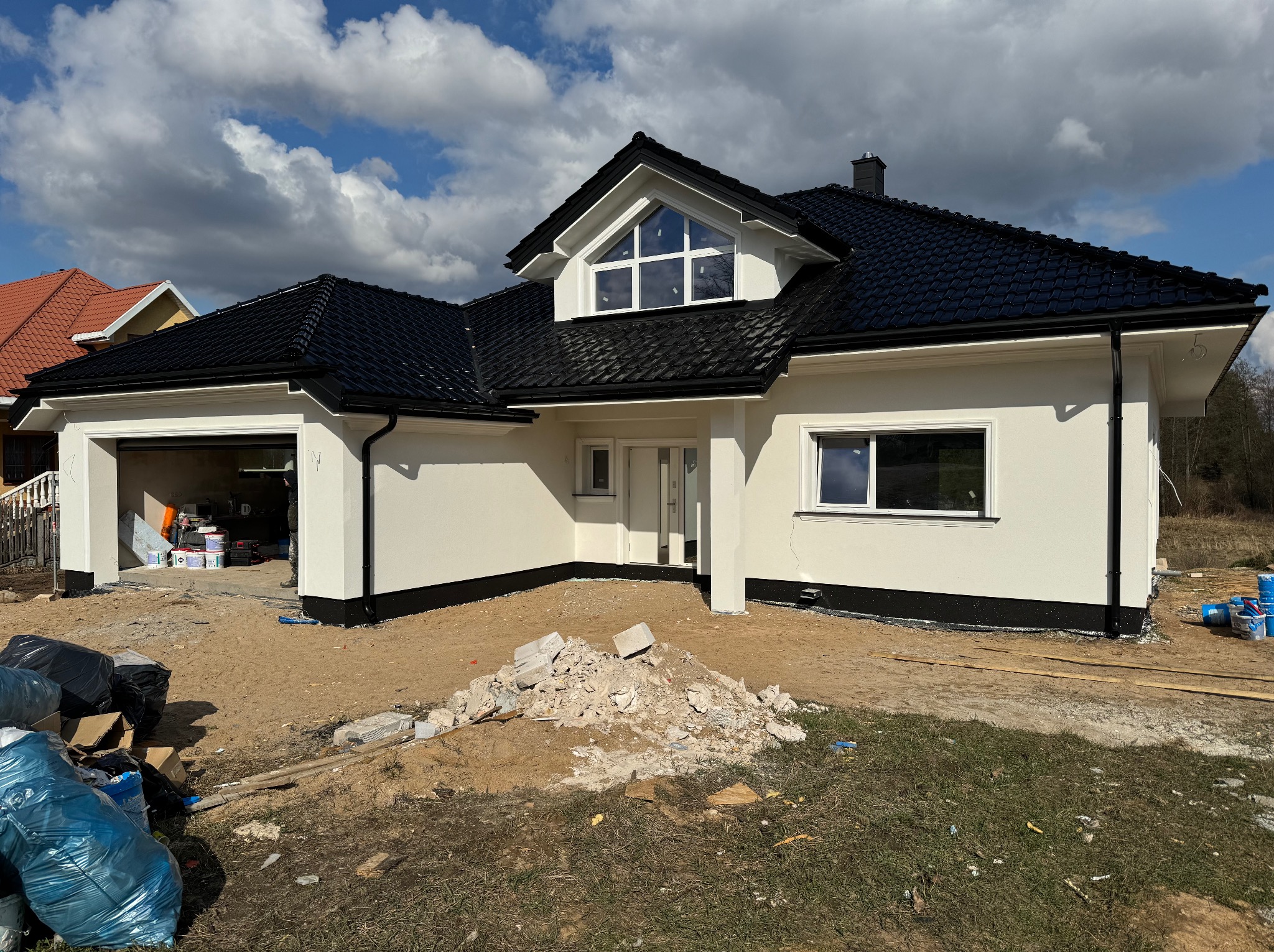 Nowoczesny dom jednorodzinny z białą elewacją i czarnym dachem w Białymstoku. Widoczne ślady prac wykończeniowych wokół budynku, co sugeruje świeżo zakończony etap budowy.