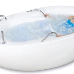 doMASAZU.pl fotele masujące - łóżka do masażu - sprzęt reha - Uśmiechnięta kobieta relaksuje się w białej wannie z hydromasażem, woda z bąbelkami, chromowane uchwyty i panele sterowania. Zabieg spa.