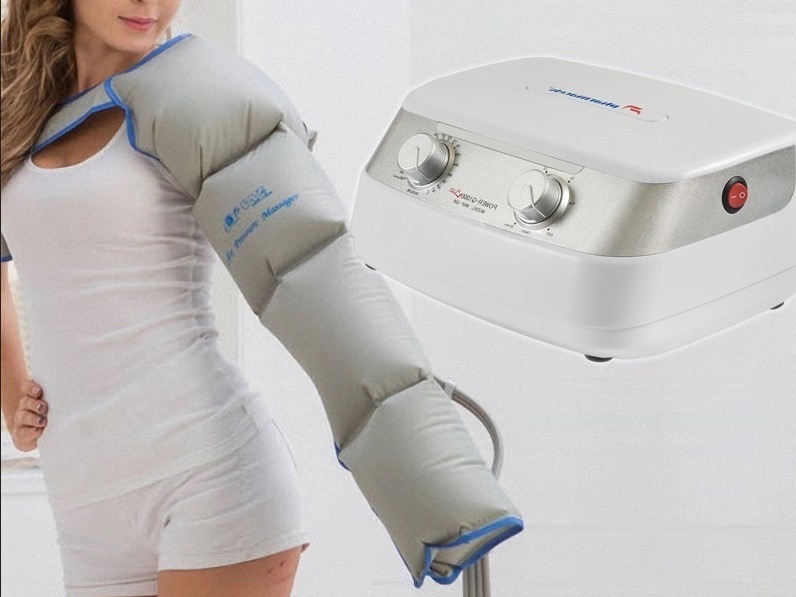 Aparat do masażu pneumatycznego na ramieniu kobiety w białym topie i spodenkach, z widocznym urządzeniem sterującym na jasnym tle.