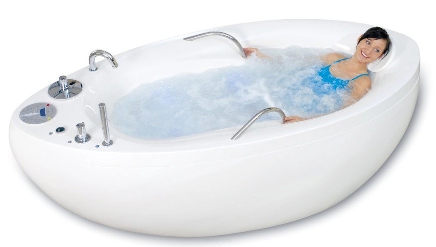 Uśmiechnięta kobieta relaksuje się w białej wannie z hydromasażem, woda z bąbelkami, chromowane uchwyty i panele sterowania. Zabieg spa.