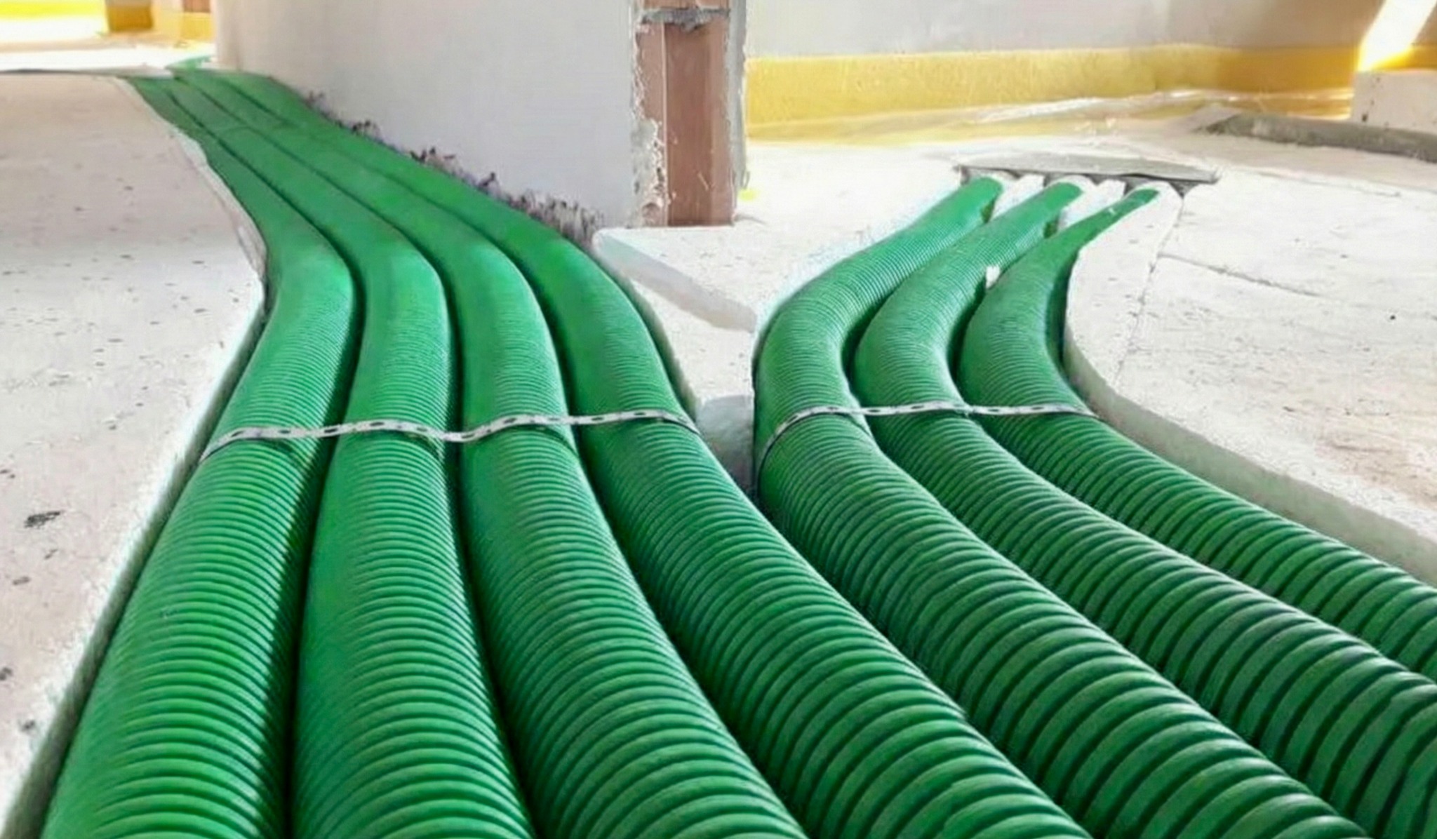 Zielone, karbowane rury wentylacyjne ułożone w bruzdach w podłodze, zabezpieczone metalowymi klamrami, gotowe do zalania wylewką. Instalacja w trakcie realizacji.