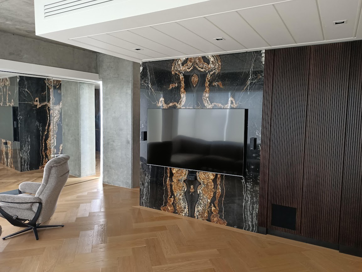 Elegancki salon w Mińsku Mazowieckim z akcentami z czarnego kamienia z unikalnym, złotym wzorem na ścianie za telewizorem i obudowie przejścia.