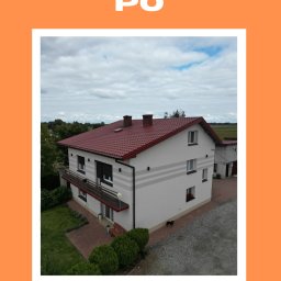 Gentle-Investments - Dom po remoncie elewacji i dachu, widok z góry. Czerwona dachówka, jasna elewacja z szarymi pasami. Mały czarny pies na podwórku. Zdjęcie z napisem 'PO'.