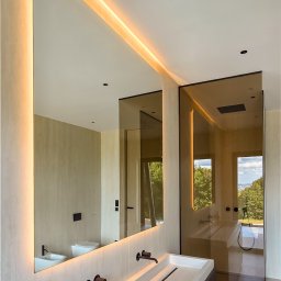 Glasco Sp. z o.o. - Nowoczesna łazienka z podświetlanym lustrem i kabiną prysznicową ze szkła barwionego w masie. Minimalistyczny design, armatura w kolorze czarnym.