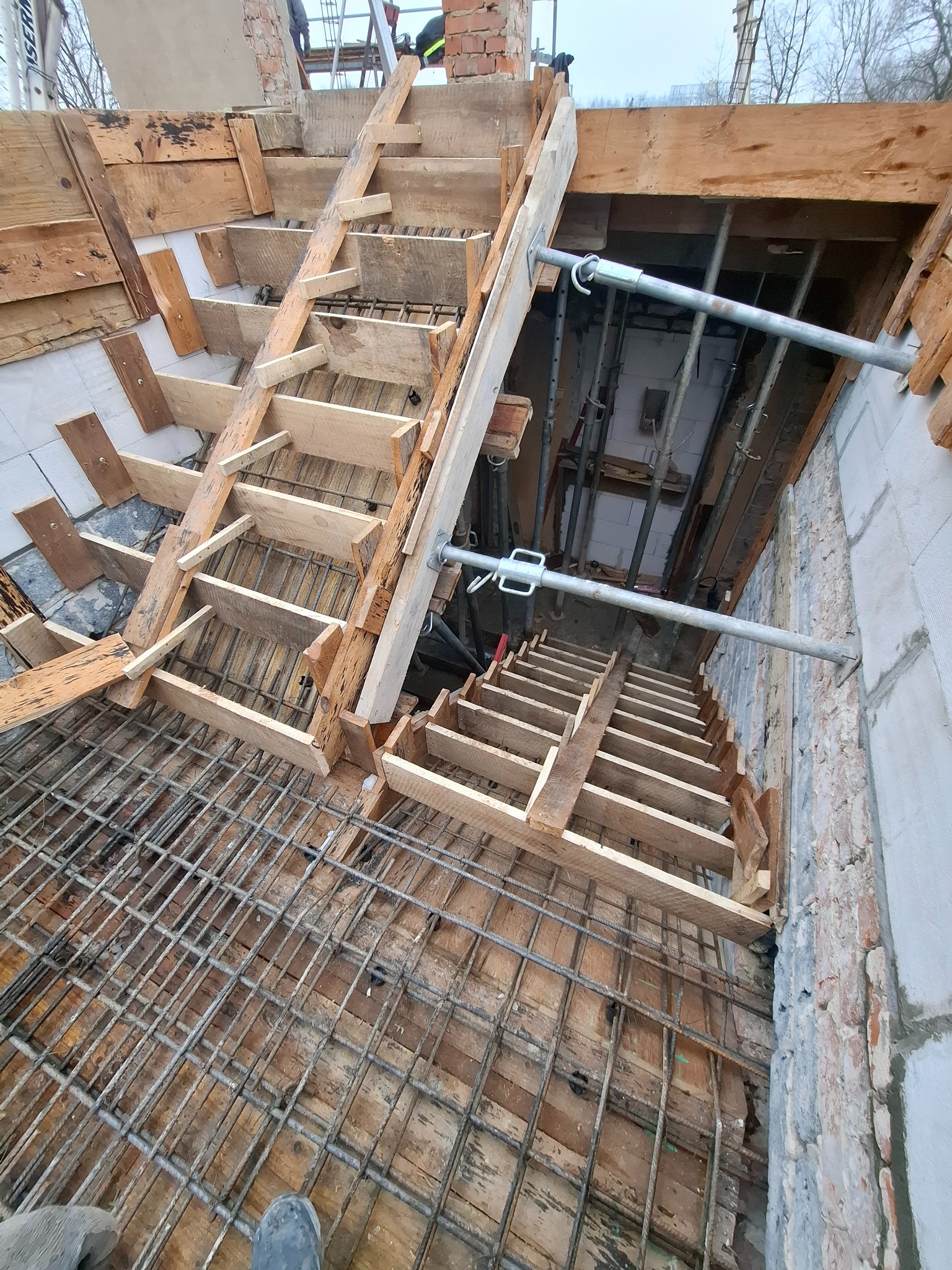 Zbrojenie i szalunek schodów na budowie domu. Widoczne drewniane elementy konstrukcyjne i stalowe pręty zbrojeniowe. Ujęcie z góry, ukazujące detale wykonania.