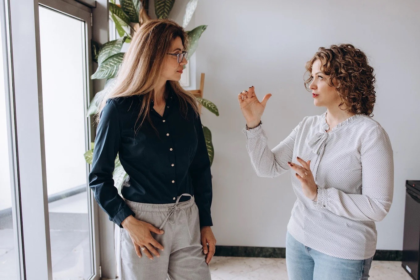Dwie kobiety w jasnym wnętrzu, jedna gestykuluje, prowadząc rozmowę lub prezentację, sugerując interaktywny charakter szkolenia.