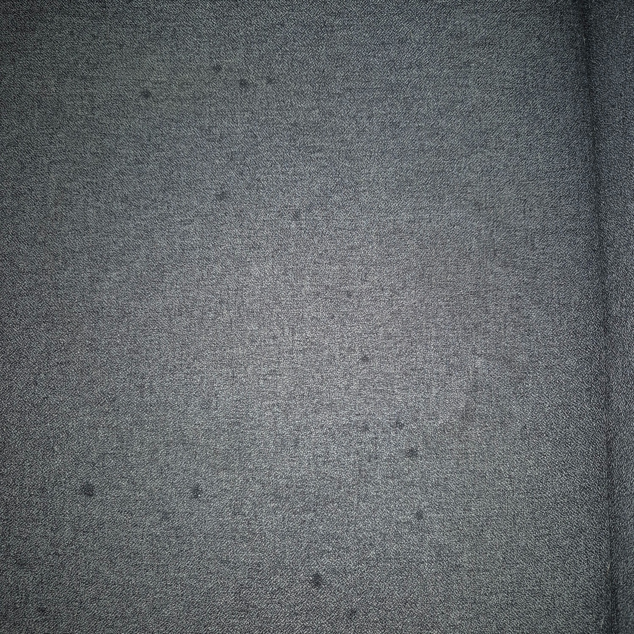 Szary materiał tekstylny o drobnej fakturze, widoczne delikatne plamy. Materiał przypomina tapicerkę meblową lub dywan.