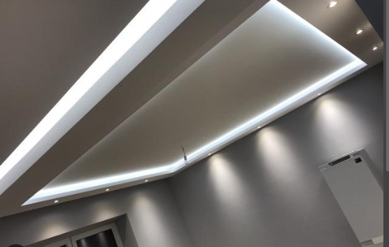 Nowoczesny sufit podwieszany z oświetleniem LED w kształcie prostokąta, uzupełniony punktowymi lampami. Szare ściany i fragment okna w dolnym rogu.