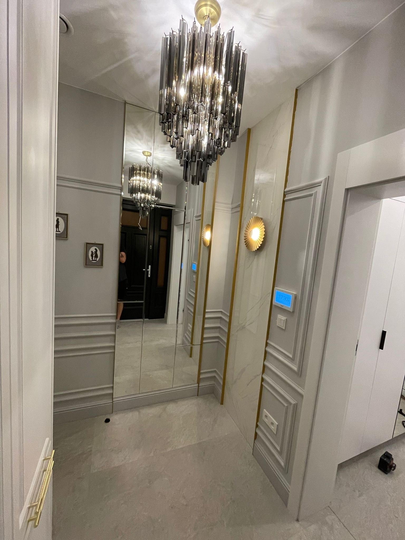 Elegancki przedpokój z lustrami, dekoracyjnymi panelami ściennymi i nowoczesnym oświetleniem. Widoczne detale wykończenia i subtelna kolorystyka.