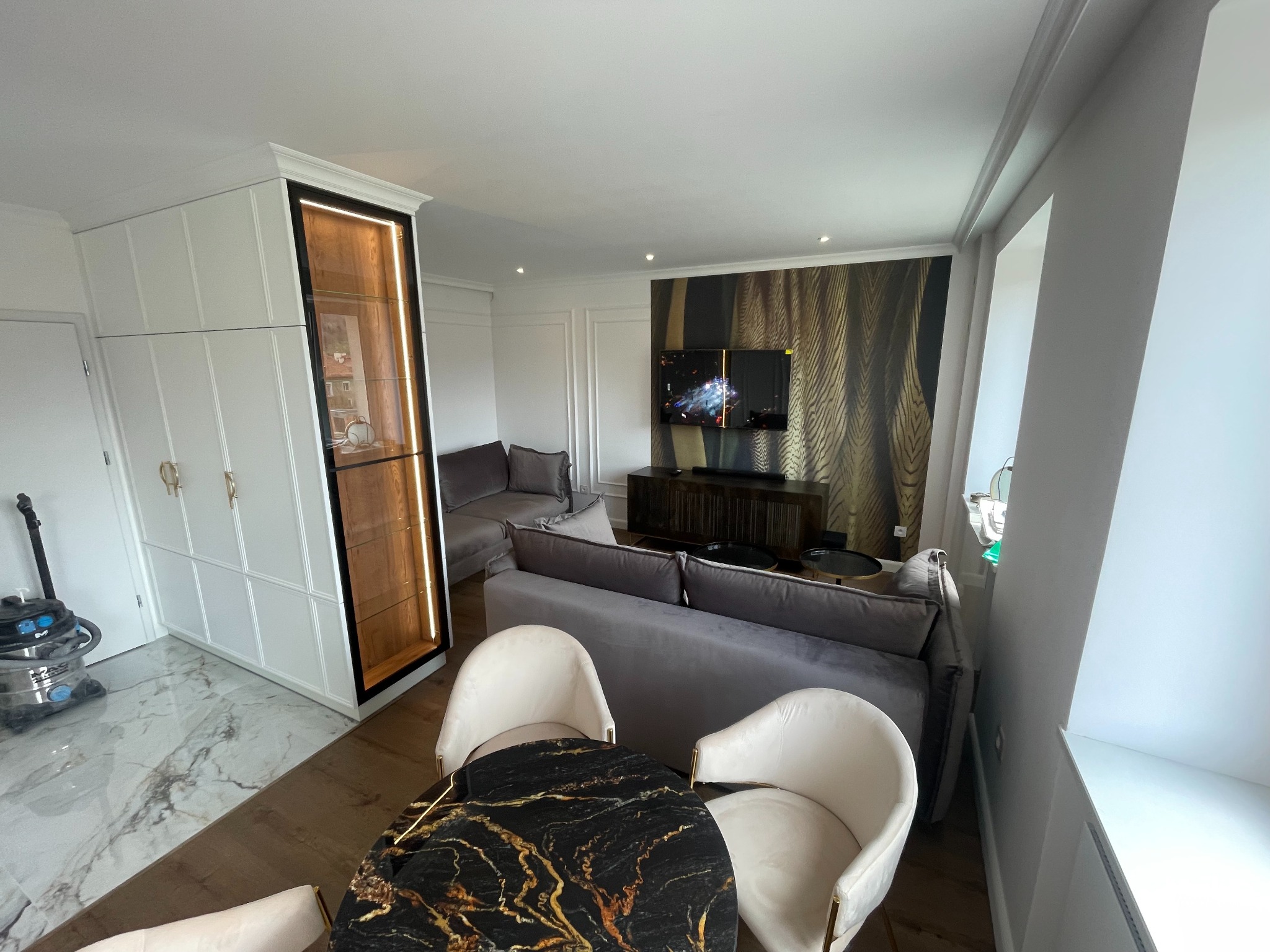 Eleganckie wykończenie wnętrza salonu z marmurową podłogą, szafą z podświetleniem i okrągłym stołem z blatem imitującym czarny marmur. Nowoczesny design.