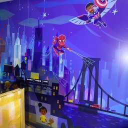 FP CONSTRUCTION - Kolorowa grafika ścienna w pokoju dziecięcym: Spiderman, Falcon, Brooklyn Bridge i panorama miasta w fioletowo-niebieskiej tonacji. W tle widoczne kartony i elementy wyposażenia.