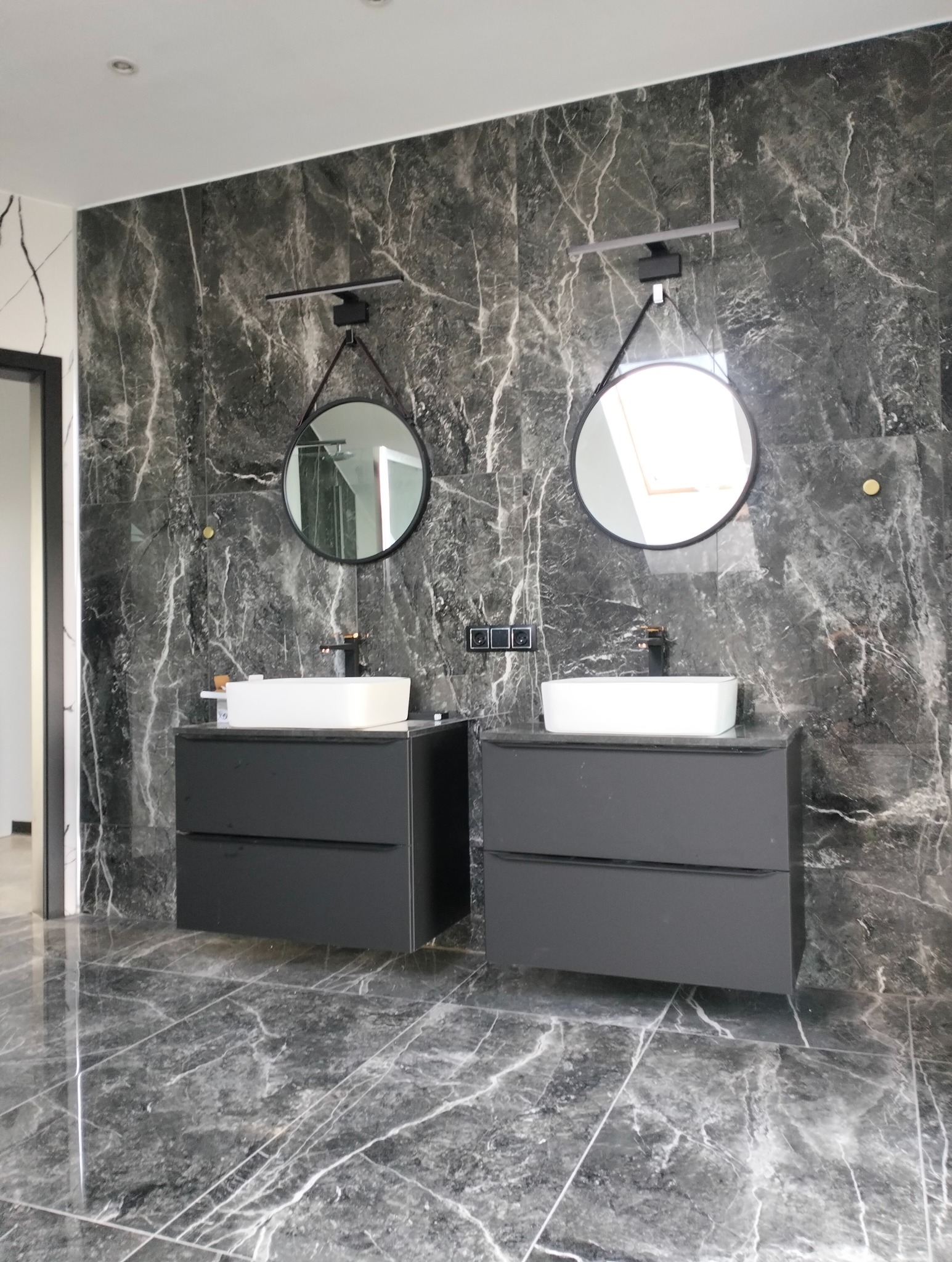 Elegancka łazienka z dwoma umywalkami na tle ściany i podłogi z płytek imitujących marmur. Okrągłe lustra z oświetleniem nadają wnętrzu nowoczesny charakter.