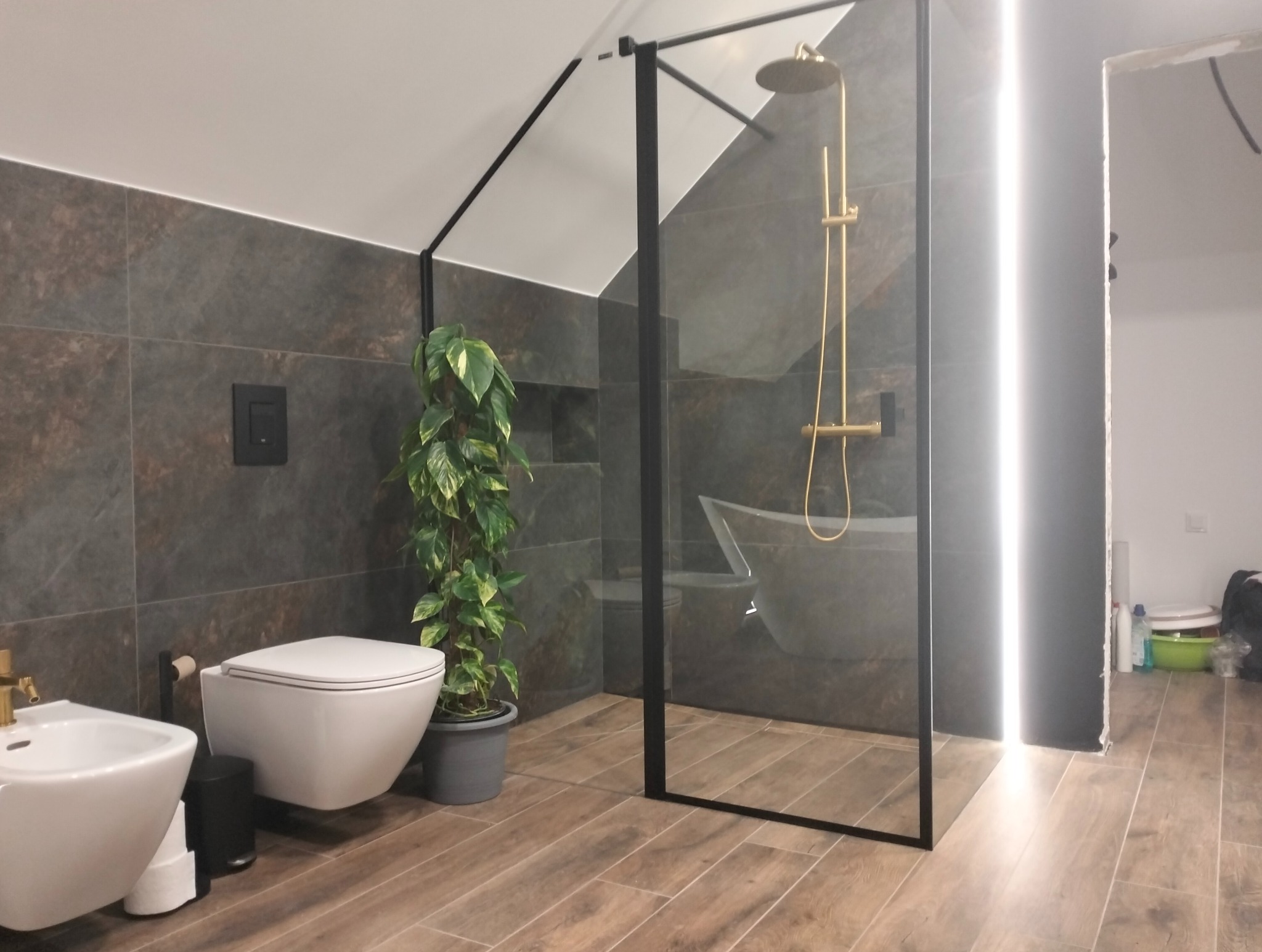 Nowoczesna łazienka w Stargardzie z kabiną prysznicową typu walk-in, brązowymi płytkami imitującymi drewno i wiszącą toaletą. Uwagę przykuwa złota armatura.