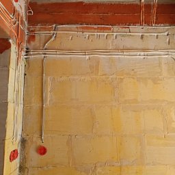 WOJ-TECH Wojciech Świderski - Ściana z widoczną instalacją elektryczną w trakcie montażu: kable prowadzone w bruzdach, puszki podtynkowe. Surowy stan, cegła i beton.