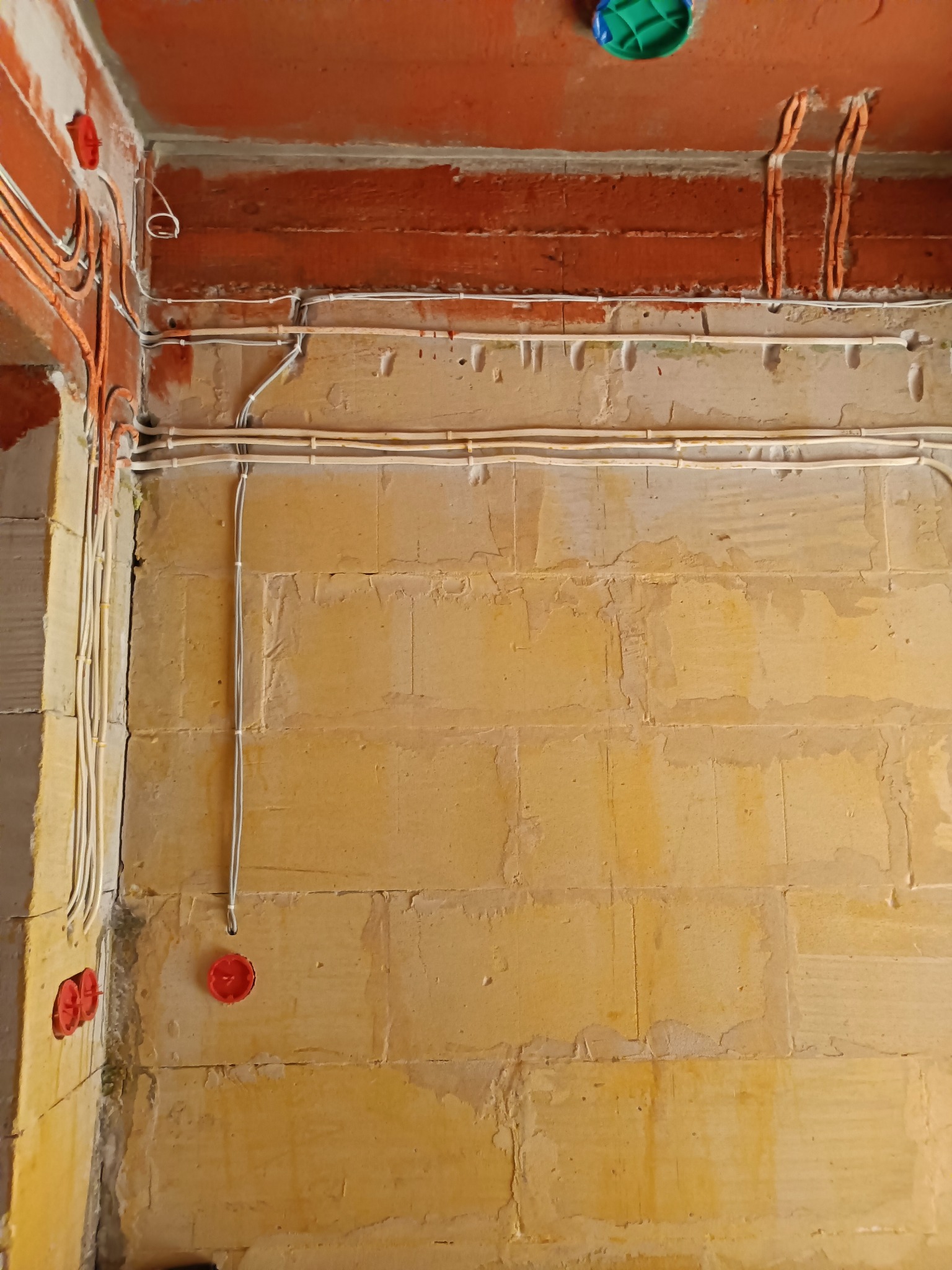 Ściana z widoczną instalacją elektryczną w trakcie montażu: kable prowadzone w bruzdach, puszki podtynkowe. Surowy stan, cegła i beton.