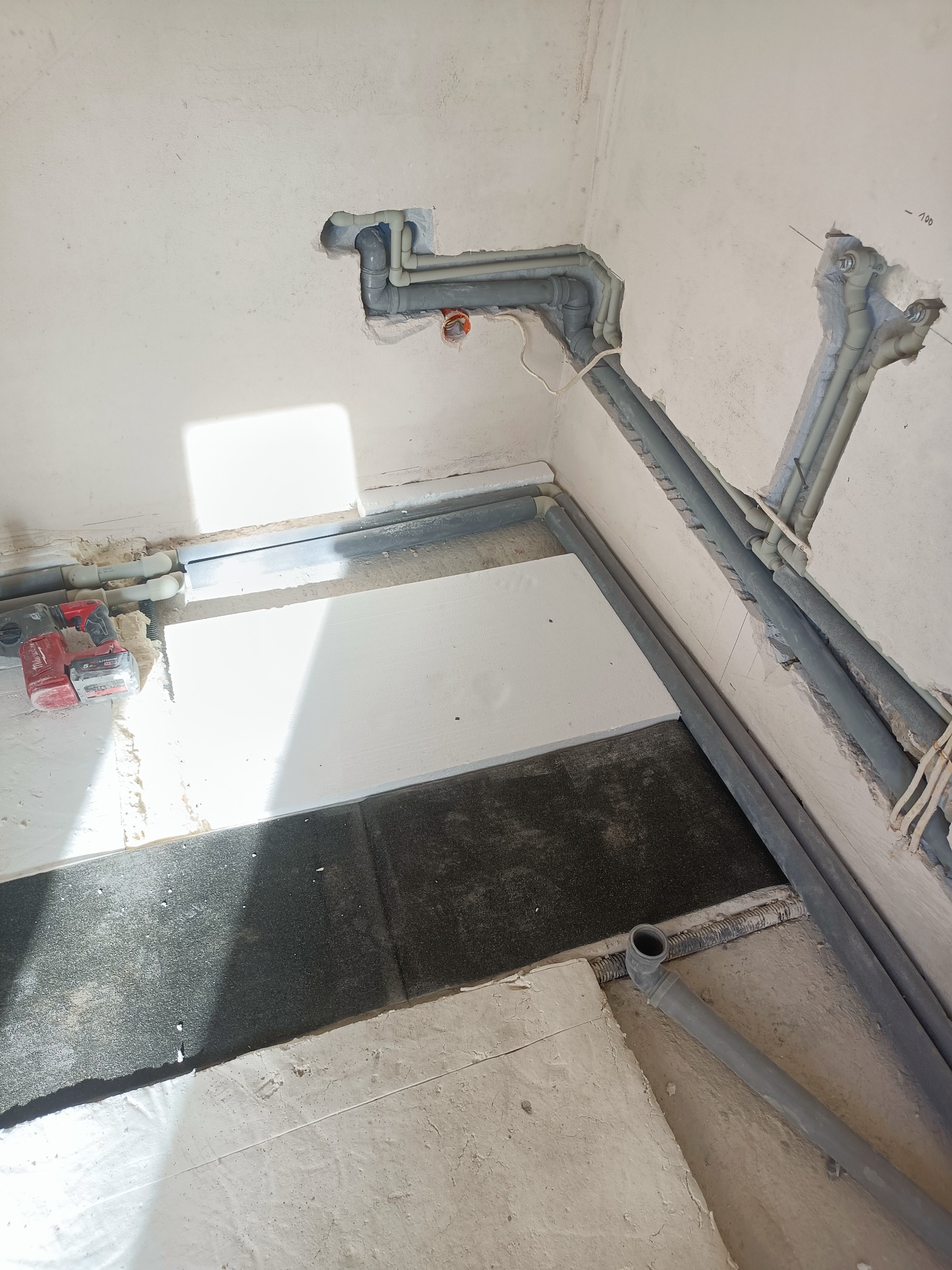 Szare rury instalacji hydraulicznej zamontowane w ścianie i podłodze w Kosowie Lackim, widoczne narzędzia. Etap prac przed zakryciem instalacji.