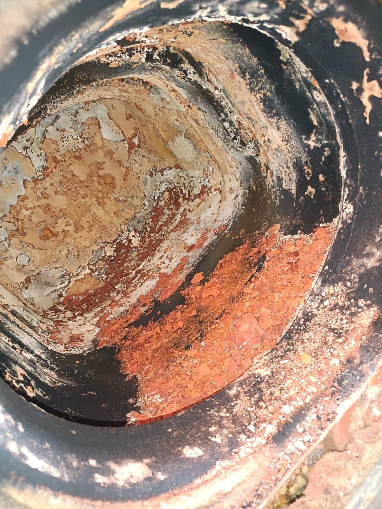 Wnętrze skorodowanej rury kanalizacyjnej z widocznymi śladami rdzy i osadów, sfotografowane z góry pod kątem, ukazujące stopień zużycia i potrzebę wymiany.