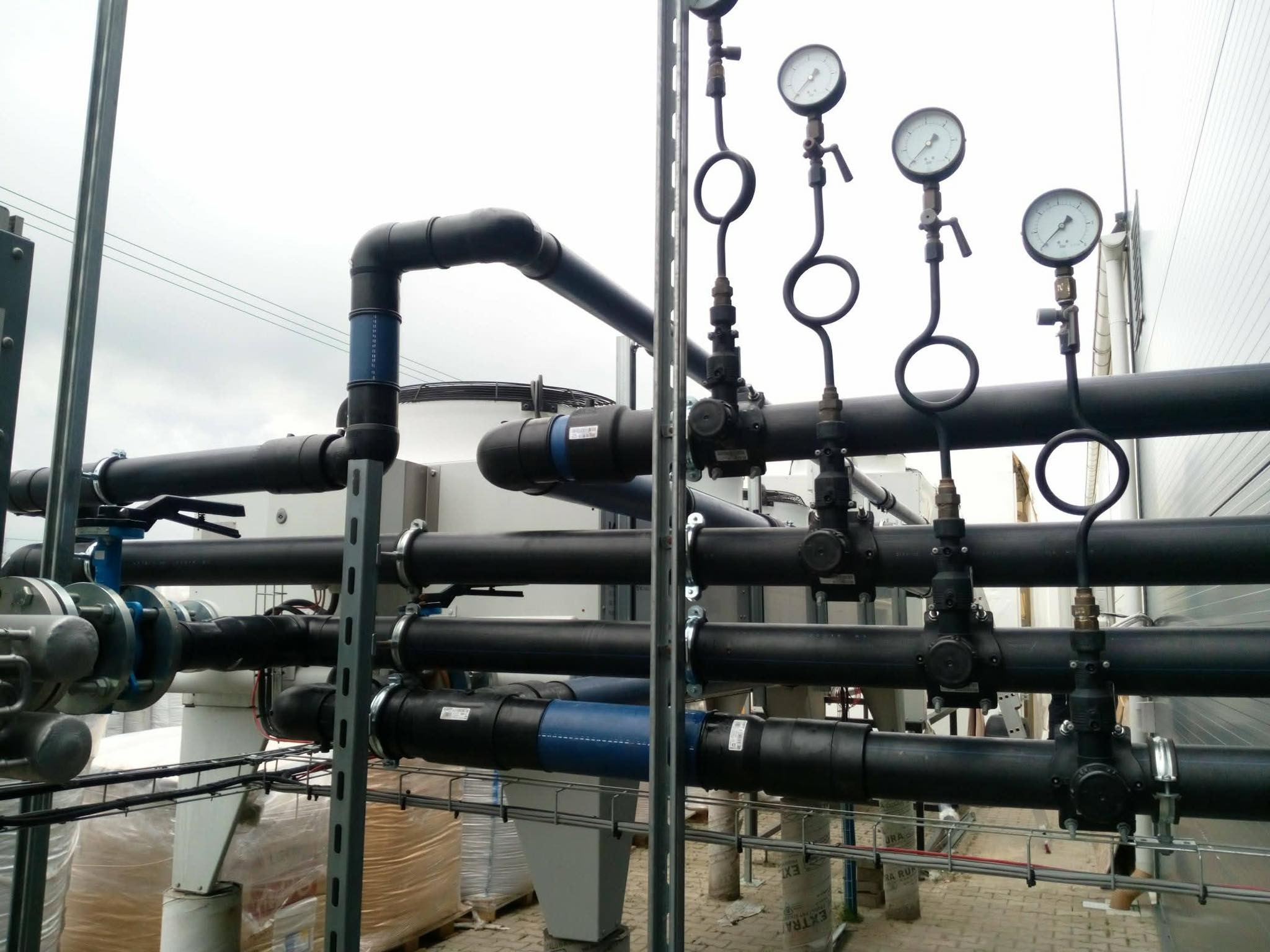 Kompleksowa instalacja przemysłowa z czarnych rur, zaworów i manometrów, zamontowana na metalowej konstrukcji wsporczej wewnątrz budynku.
