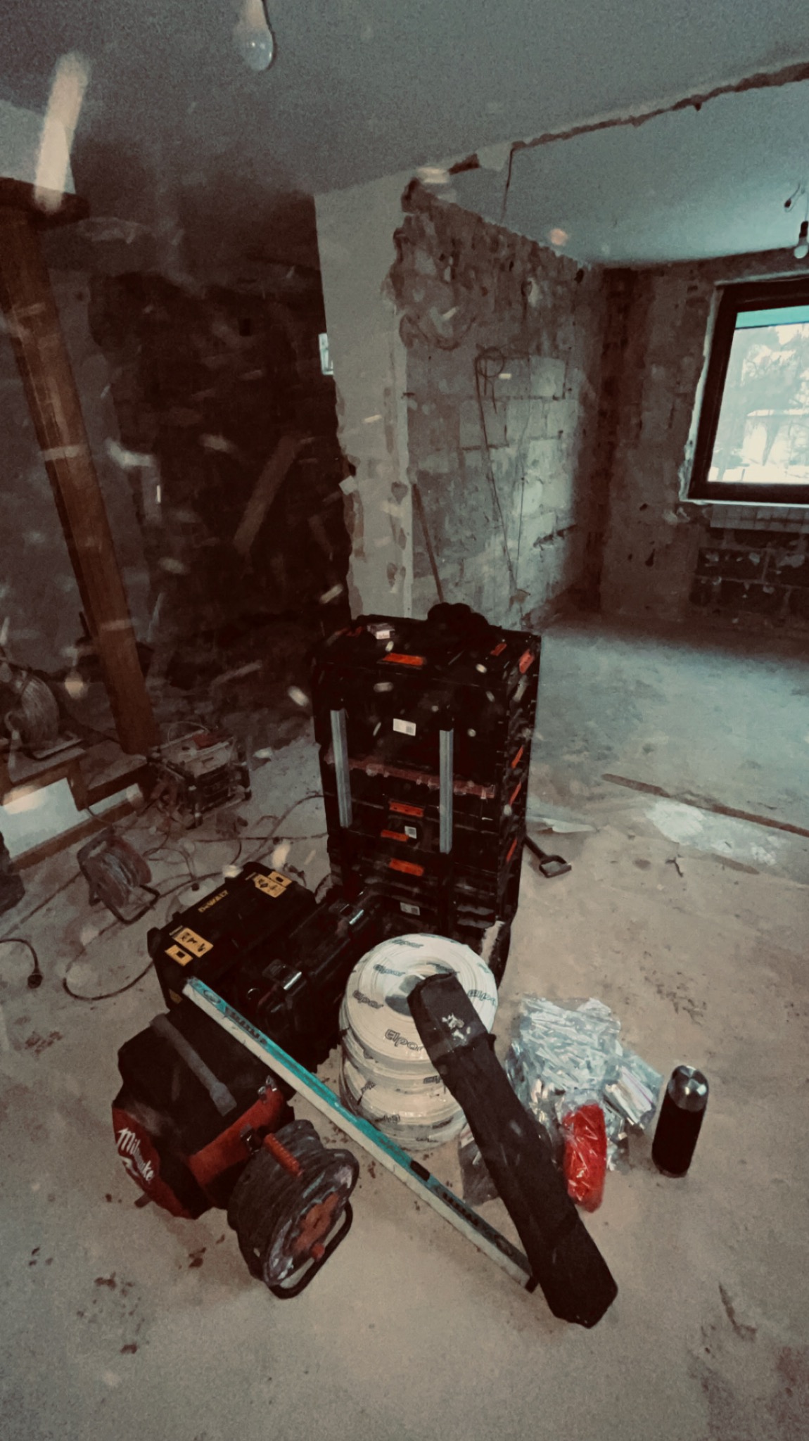 Remontowane wnętrze z narzędziami: skrzynki, zwój kabli, poziomica. Widoczne ślady po kuciu ścian, surowy stan wykończenia. Przygotowania do prac instalacyjnych.