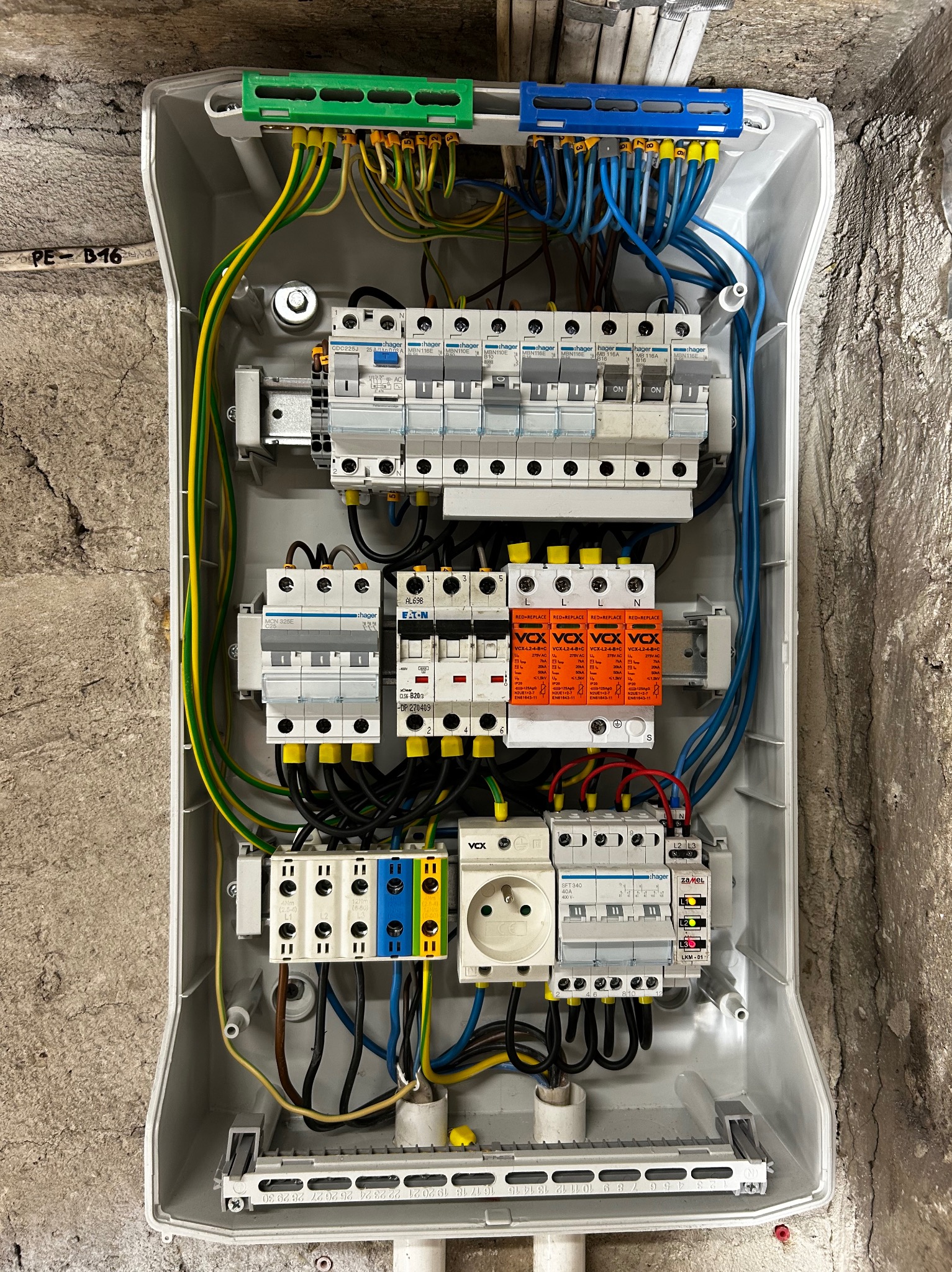 Rozdzielnica elektryczna z zainstalowanymi zabezpieczeniami, widoczne przewody w kolorach: niebieskim, żółto-zielonym i brązowym. Elementy marki Hager i Eaton.