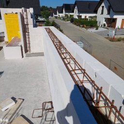 MaxBud Maksym Maruda - Wznoszenie ścian z betonu komórkowego Ytong z widocznym zbrojeniem wewnątrz, na tle zabudowy jednorodzinnej w słoneczny dzień.