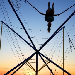 Plenerowo.com Atrakcje & Gastronomia - Dwie osoby na bungee trampolinie na tle zachodzącego słońca. Jedna osoba w powietrzu, druga skacze. Konstrukcja z lin i metalowych rurek.