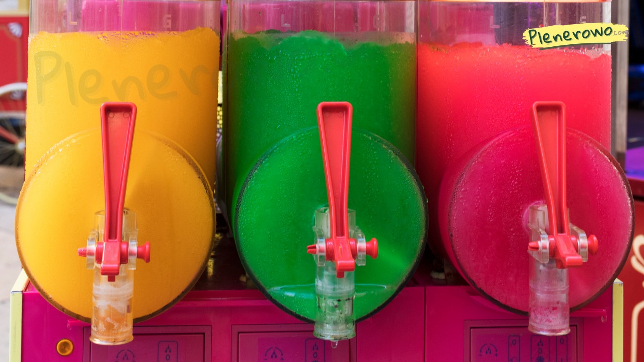 Automat do mrożonych napojów z trzema zbiornikami: żółty, zielony i czerwony. Każdy z czerwonym kranikiem. Widoczne krople kondensacji na zbiornikach.