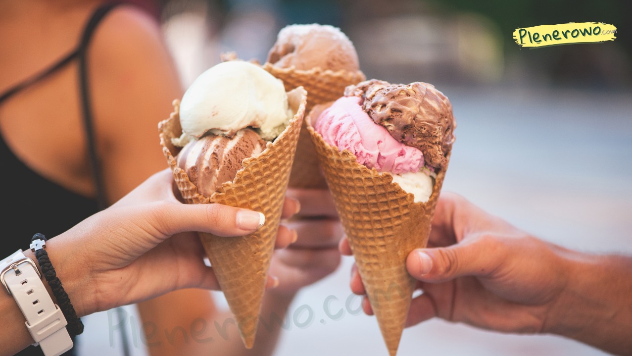 Trzy rożki lodowe o różnych smakach trzymane przez osoby na tle rozmytym. Lody waniliowe, czekoladowe i różowe w waflowych rożkach.