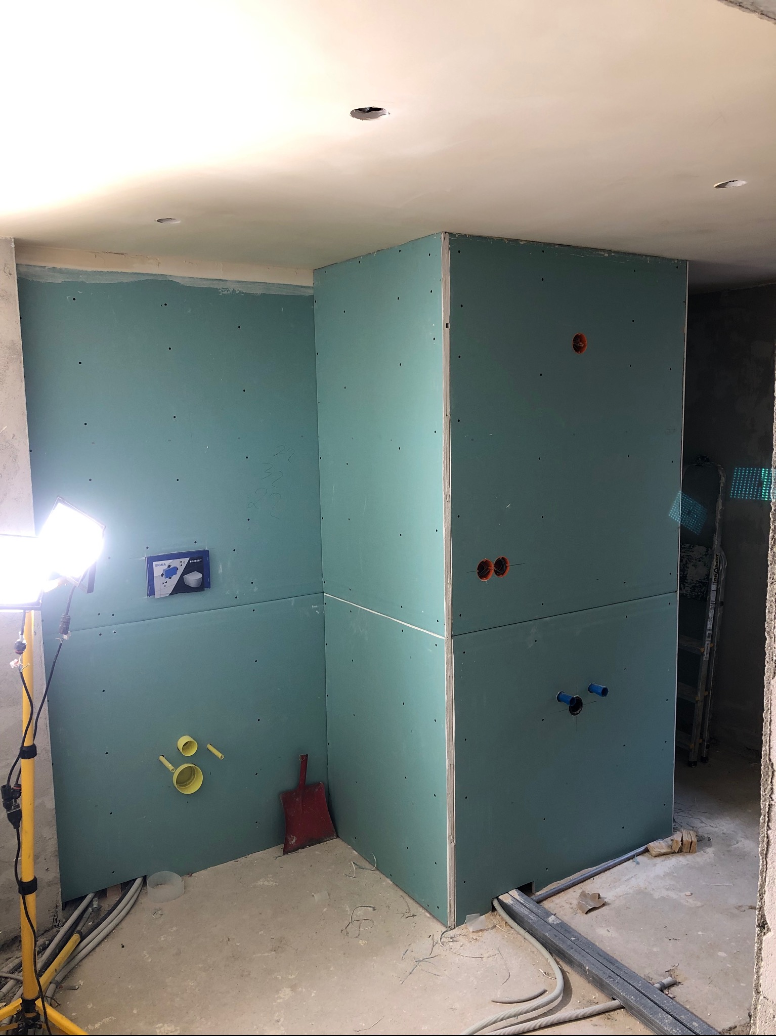 Łazienka w trakcie zabudowy z płyt karton-gips, widoczne instalacje wodno-kanalizacyjne i oświetlenie robocze. Ściany przygotowane do dalszych prac wykończeniowych.