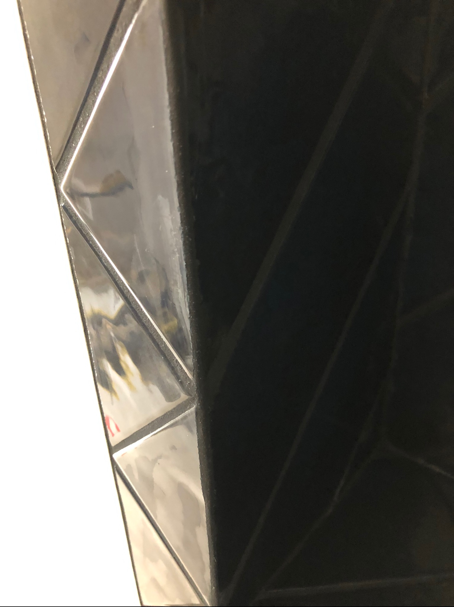 Błyszcząca, czarna, trójkątna mozaika ścienna z wyraźnymi fugami, ułożona pod kątem, z fragmentem białej ściany po lewej stronie kadru.