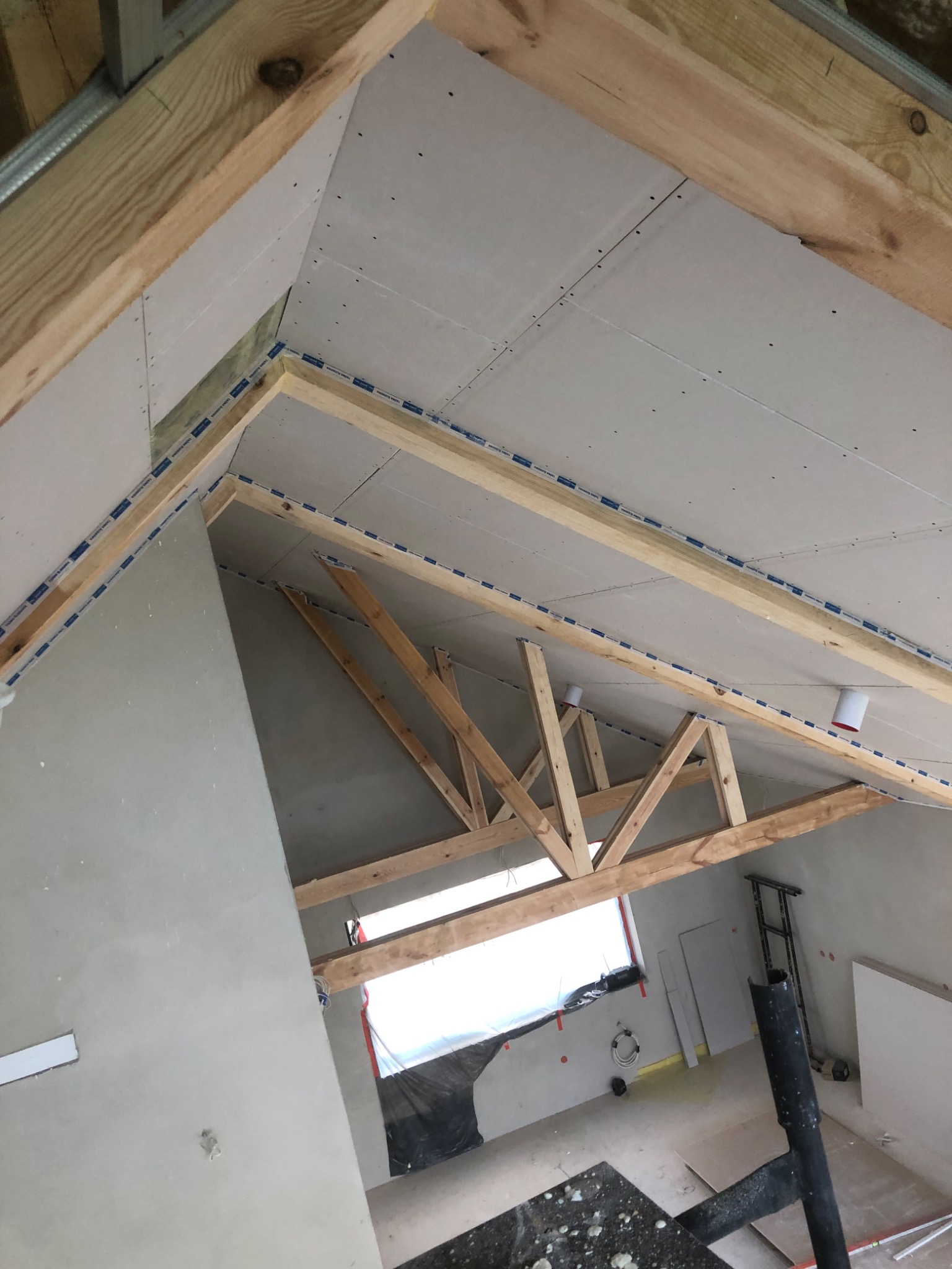 Poddasze w trakcie wykańczania: drewniana konstrukcja dachu, płyty karton-gips na skosach, widoczne łączenia płyt, okno dachowe. Prace wykończeniowe w toku.