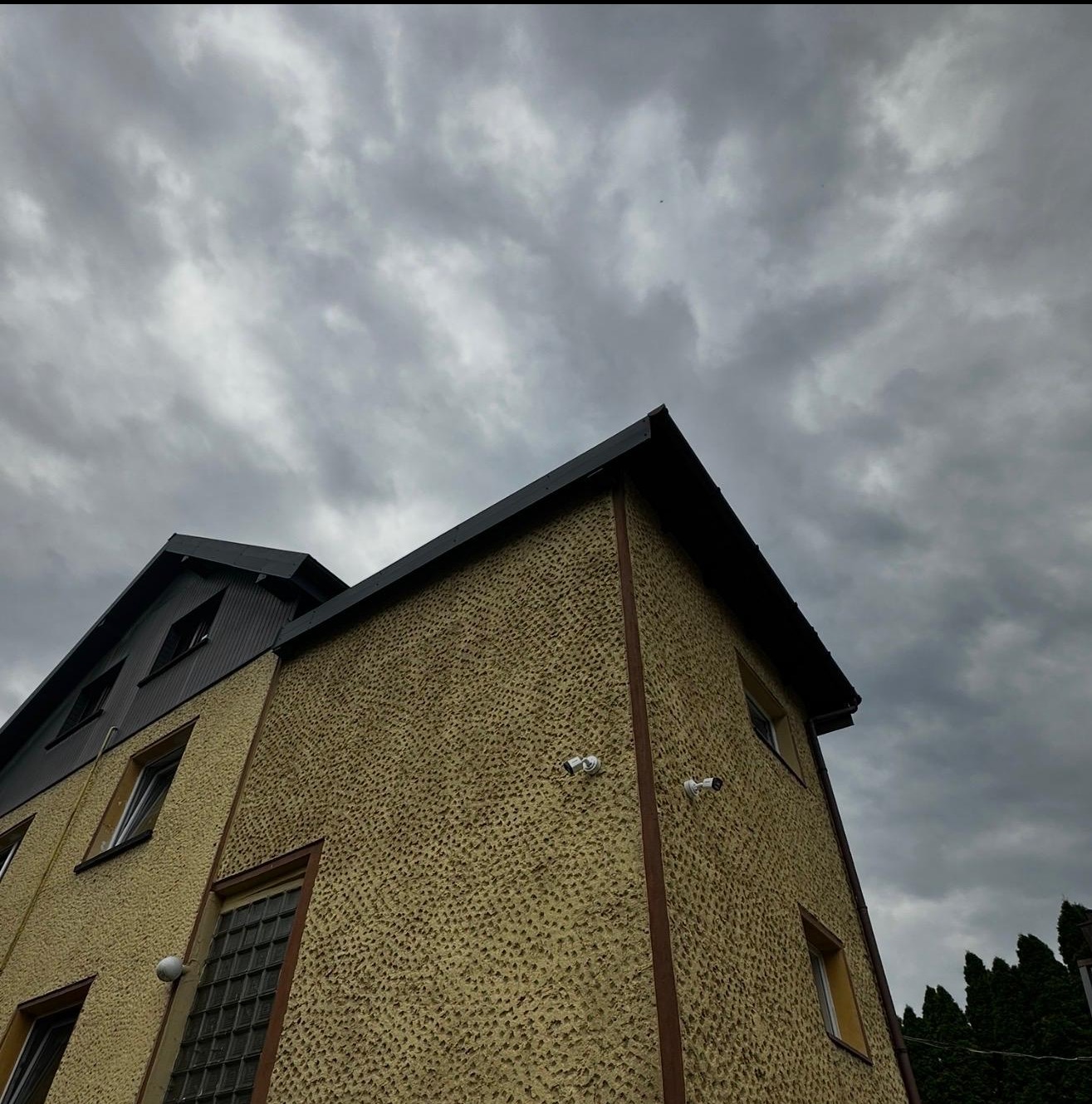 Budynek z zamontowanymi kamerami monitoringu na elewacji, sfotografowany pod kątem, z widocznym pochmurnym niebem w tle. Dwie kamery na ścianie.
