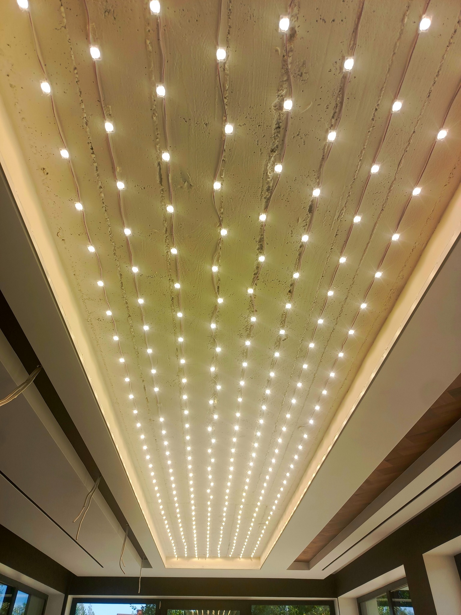 Nowoczesny sufit z równomiernie rozmieszczonymi punktami LED, tworzącymi unikalny efekt oświetleniowy. Widoczne przewody i surowa faktura sufitu.