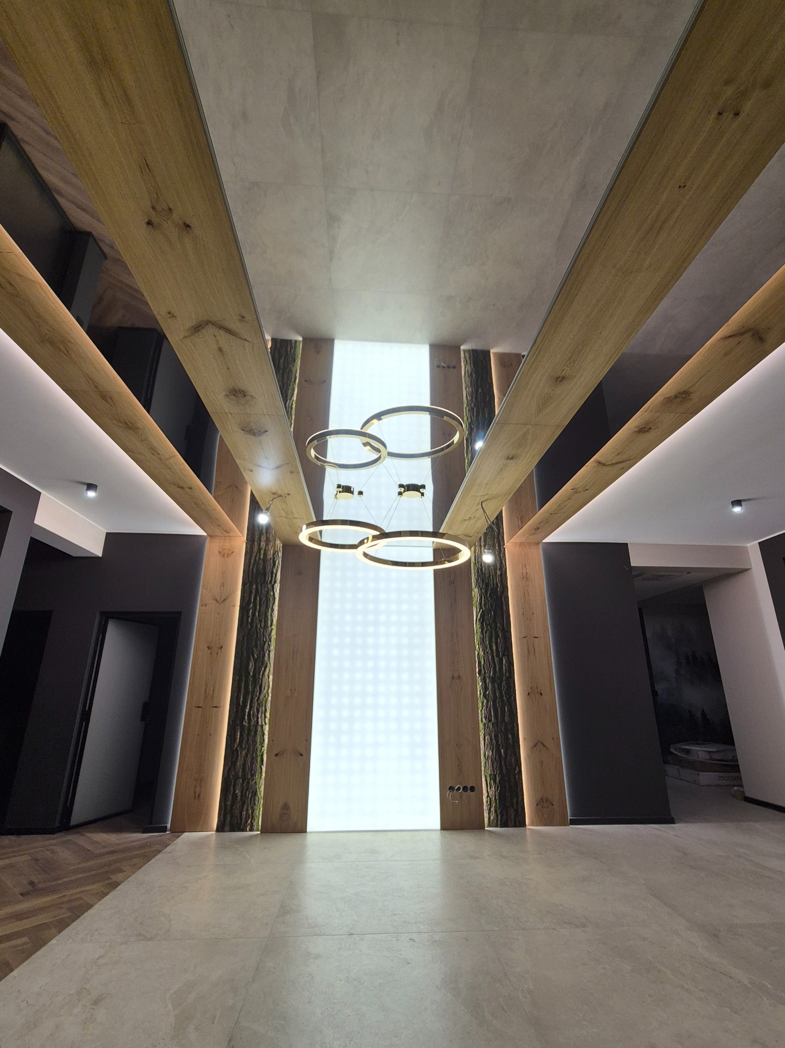 Nowoczesne oświetlenie sufitowe z trzema okrągłymi lampami LED, drewniane belki i panele z efektem kory drzewa, subtelne punkty świetlne wkomponowane w architekturę wnętrza.