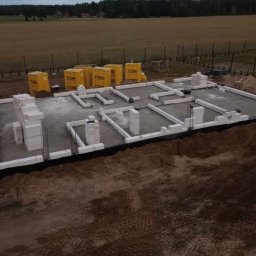 kacper łazarowicz - Fundamenty domu z bloczków Ytong w Krajenka, widok z góry. Częściowo wymurowane ściany nośne, izolacja przeciwwilgociowa. W tle pole i las.