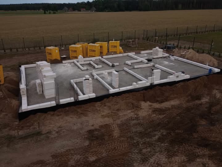 Fundamenty domu z bloczków Ytong w Krajenka, widok z góry. Częściowo wymurowane ściany nośne, izolacja przeciwwilgociowa. W tle pole i las.