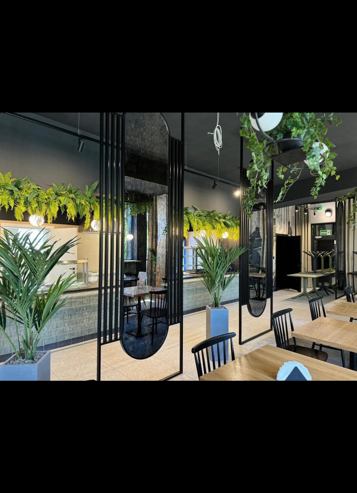 Nowoczesne wykończenie wnętrza restauracji w Gostyninie. Czarne elementy dekoracyjne, rośliny doniczkowe i wiszące, drewniane stoły z czarnymi krzesłami.