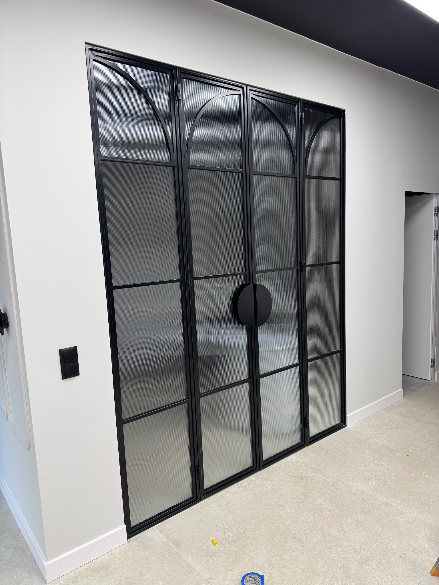 Nowoczesne, czarne, przeszklone drzwi wewnętrzne z okrągłymi uchwytami, wkomponowane w białą ścianę. Widoczny fragment podłogi i listwy przypodłogowej.
