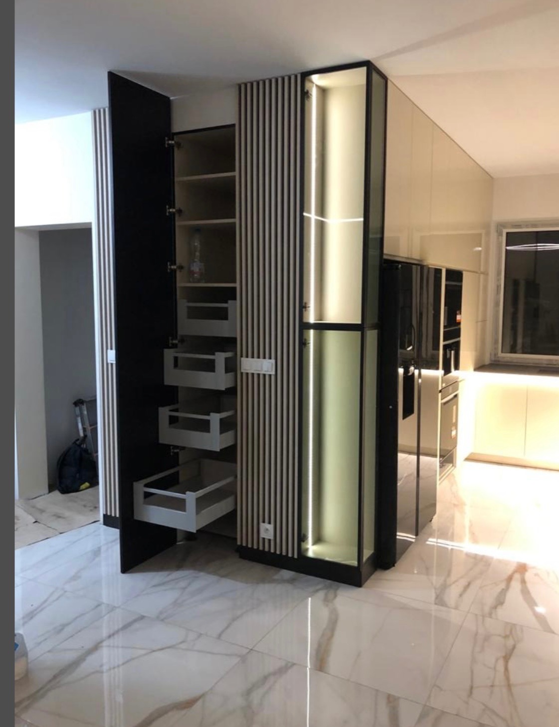 Nowoczesna zabudowa kuchenna z otwartą szafką cargo i podświetleniem LED, widoczna na tle marmurowej podłogi. Minimalistyczny design z elementami drewna.