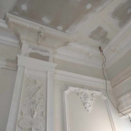 PATRYK PEJSKI - Białe, zdobione sztukaterie na ścianie i suficie w trakcie prac wykończeniowych. Widoczne ślady szpachlowania na suficie. Dekoracyjne detale architektoniczne.