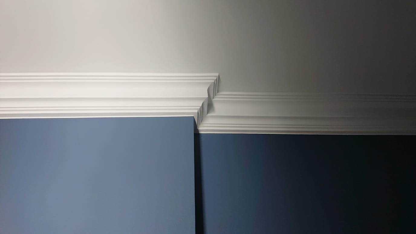 Detal wykończenia wnętrza: biała listwa dekoracyjna na styku ściany w odcieniach błękitu i sufitu. Widoczne precyzyjne łączenie elementów.