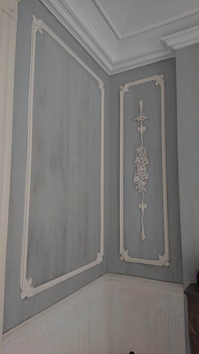 Eleganckie, szare ściany z dekoracyjnymi, białymi ramami i sztukaterią w stylu klasycystycznym. Detal wykończenia wnętrza po renowacji.