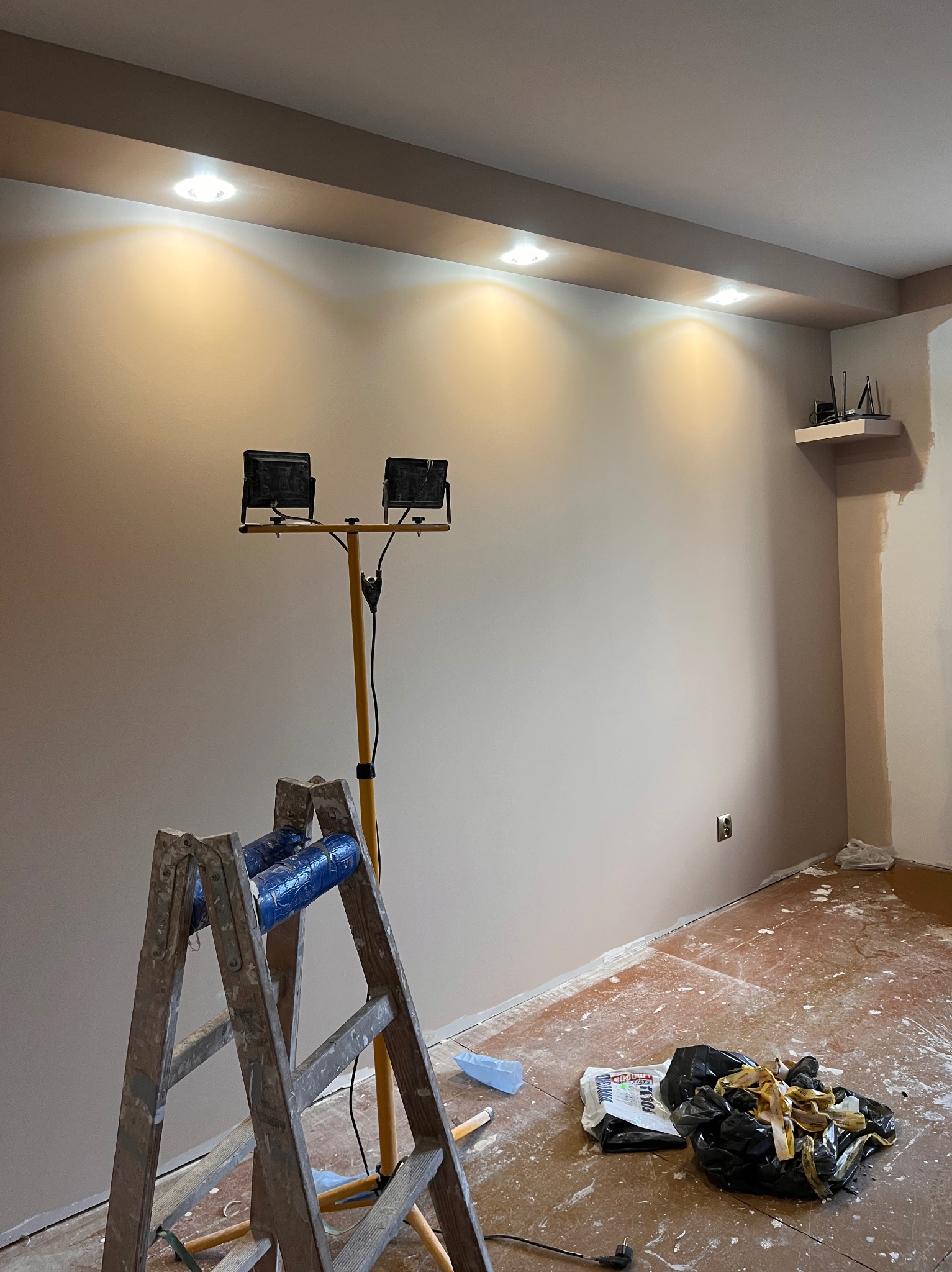 Świeżo pomalowane wnętrze z drabiną i lampą budowlaną. Widoczne detale wykończenia sufitu i gładka powierzchnia ściany w odcieniach beżu. Przygotowanie do dalszych prac.