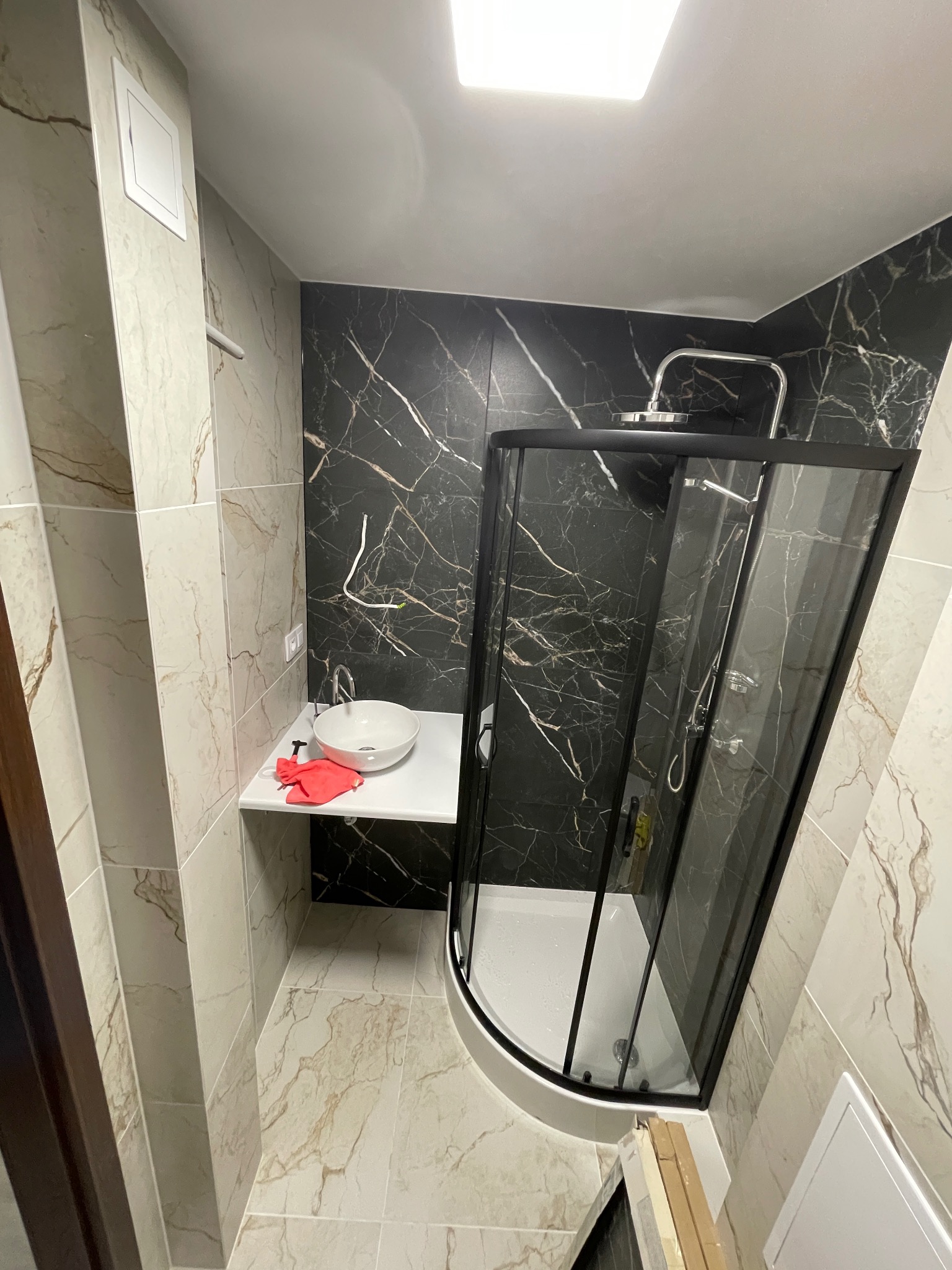 Nowoczesna łazienka po remoncie: kabina prysznicowa z czarną ramą, umywalka na blacie, marmurowe płytki w odcieniach beżu i czerni. Widoczne detale wykończenia.