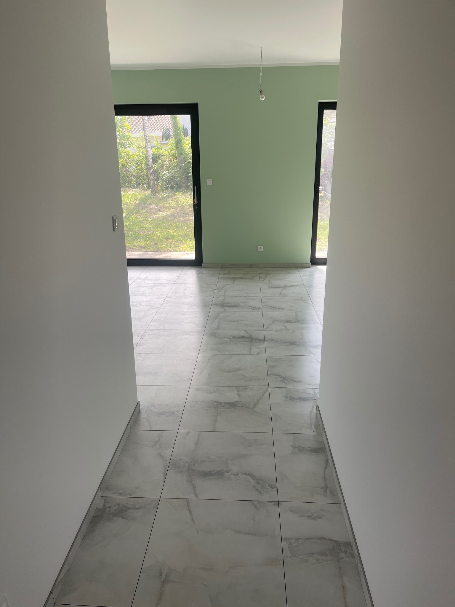 Wnętrze po remoncie: jasne płytki podłogowe imitujące marmur, świeżo pomalowane ściany na pistacjowy kolor, czarne ramy okienne. Widok z korytarza.