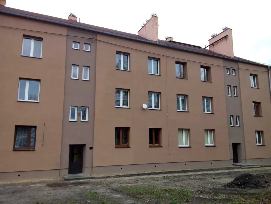 Wielorodzinny budynek po renowacji elewacji w odcieniach brązu, z widocznymi oknami o różnych rozmiarach i satelitą na ścianie. Ujęcie z poziomu gruntu.